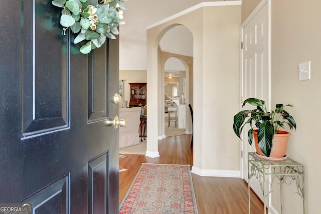 entrance foyer with baseboards, arched walkways, and wood finished floors