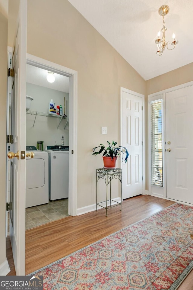 foyer featuring baseboards, a chandelier, washing machine and dryer, vaulted ceiling, and wood finished floors