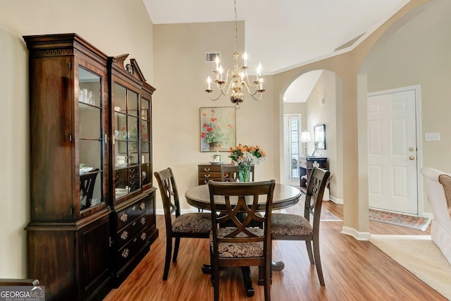 dining area with wood finished floors, visible vents, baseboards, arched walkways, and a notable chandelier