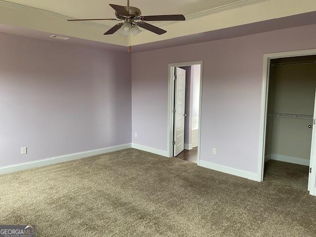 unfurnished bedroom with a closet, connected bathroom, dark colored carpet, baseboards, and a spacious closet