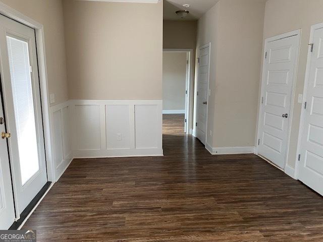 unfurnished room with dark wood finished floors, a decorative wall, and wainscoting