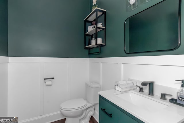 half bath with a decorative wall, wainscoting, toilet, and vanity