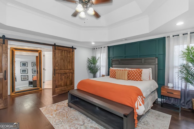 bedroom with ornamental molding, a barn door, a raised ceiling, ceiling fan, and dark wood-style flooring