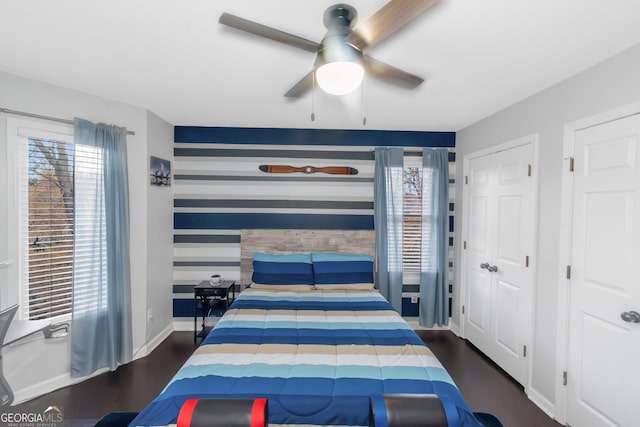 bedroom featuring multiple windows, an accent wall, baseboards, and wood finished floors