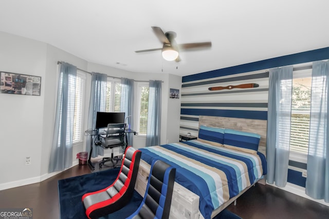 bedroom featuring an accent wall, wood finished floors, baseboards, and ceiling fan