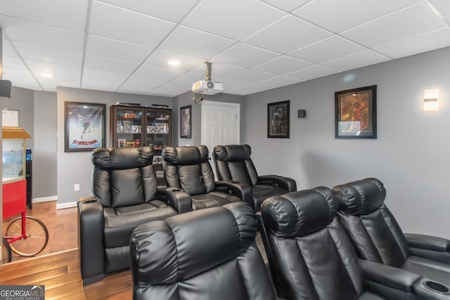 home theater room featuring wood finished floors, baseboards, and a paneled ceiling