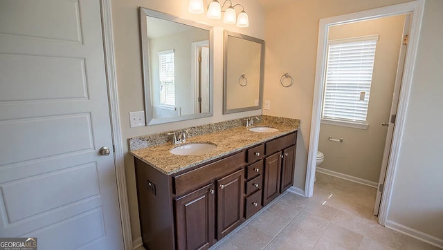 full bath featuring double vanity, toilet, baseboards, and a sink