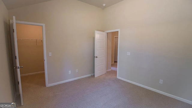 unfurnished bedroom featuring a spacious closet, baseboards, carpet, lofted ceiling, and a closet