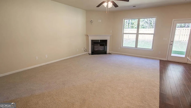 unfurnished living room featuring dark carpet, baseboards, a fireplace with flush hearth, and a ceiling fan