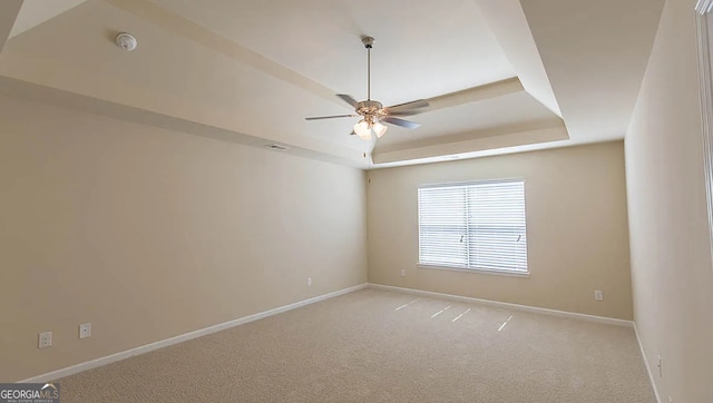 empty room with visible vents, light carpet, a ceiling fan, a tray ceiling, and baseboards