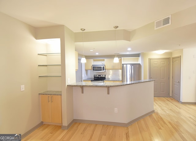 kitchen featuring a breakfast bar area, visible vents, light wood finished floors, a peninsula, and stainless steel appliances