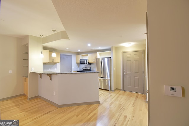 kitchen featuring light wood-type flooring, decorative light fixtures, appliances with stainless steel finishes, a peninsula, and light stone countertops