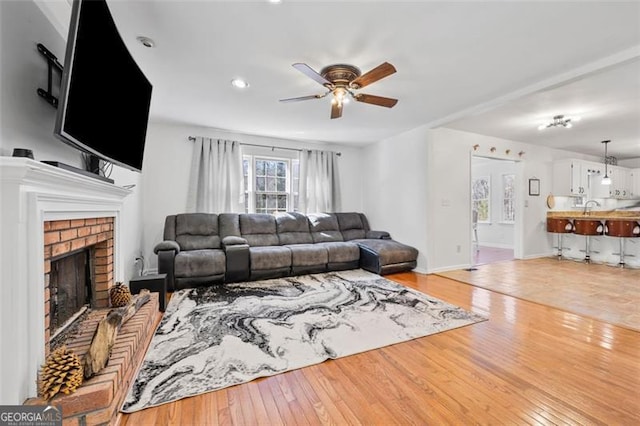 living room with baseboards, a brick fireplace, a ceiling fan, and light wood finished floors