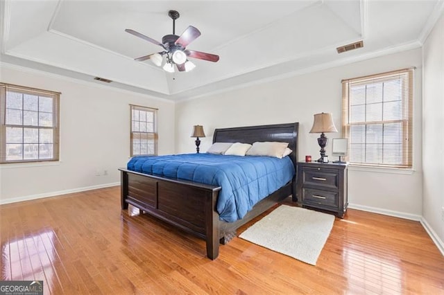 bedroom featuring visible vents, baseboards, ornamental molding, light wood-style floors, and a raised ceiling