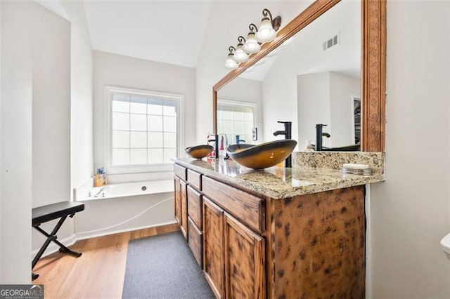 bathroom featuring visible vents, a garden tub, vaulted ceiling, wood finished floors, and vanity