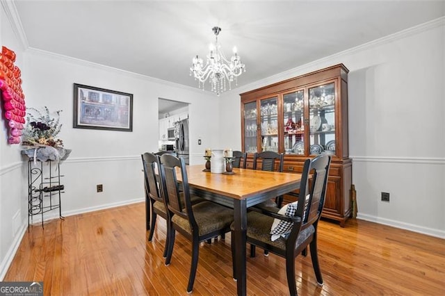 dining area featuring ornamental molding, baseboards, light wood finished floors, and a chandelier