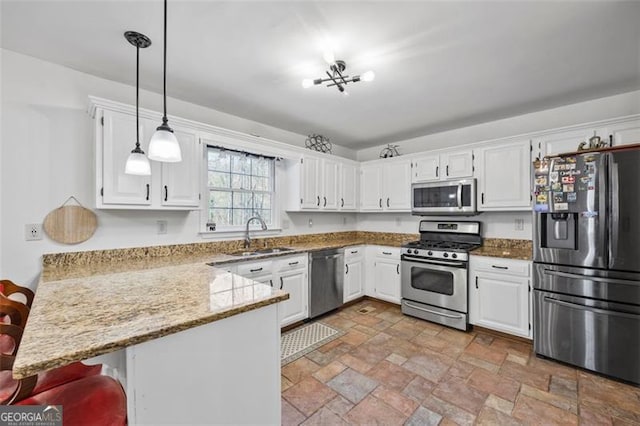 kitchen with decorative light fixtures, a peninsula, white cabinets, stainless steel appliances, and a sink