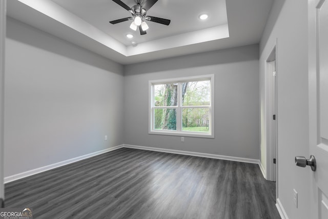 unfurnished bedroom with dark wood finished floors, recessed lighting, a raised ceiling, and baseboards