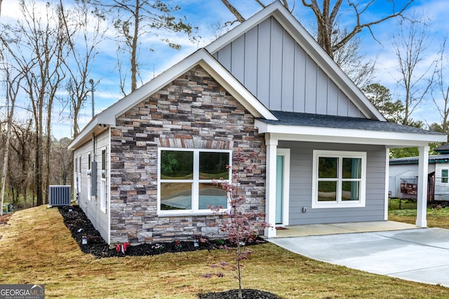 view of front of property featuring stone siding, board and batten siding, central AC, and a front yard