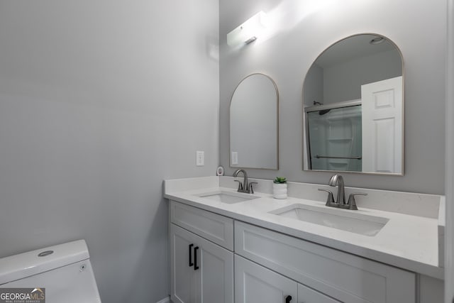 bathroom featuring double vanity, toilet, a shower with shower door, and a sink