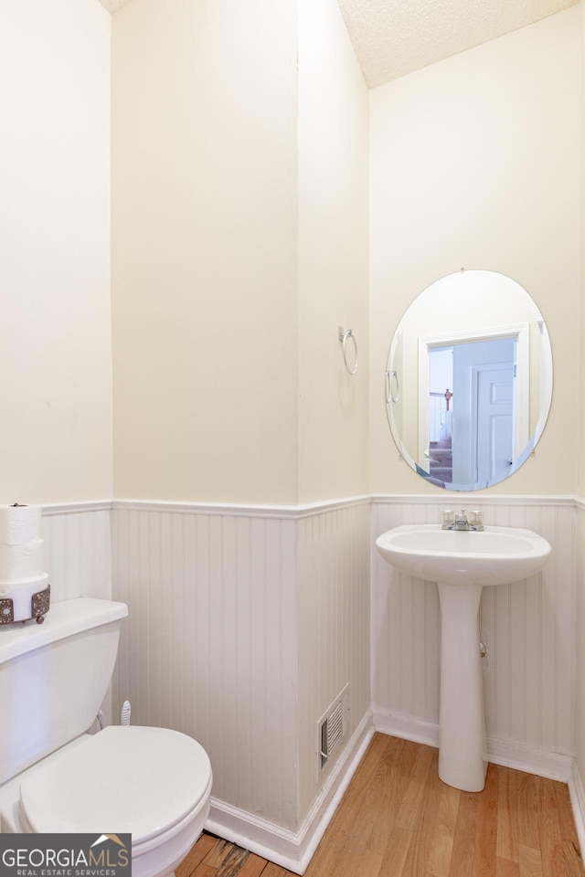 bathroom featuring visible vents, toilet, wood finished floors, and wainscoting