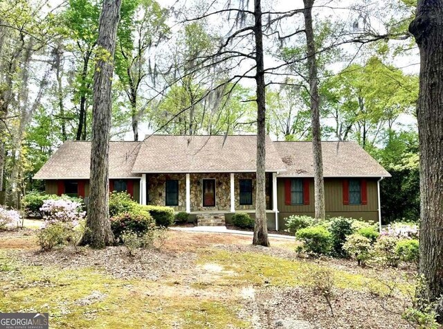 ranch-style home with stone siding, a porch, and a shingled roof