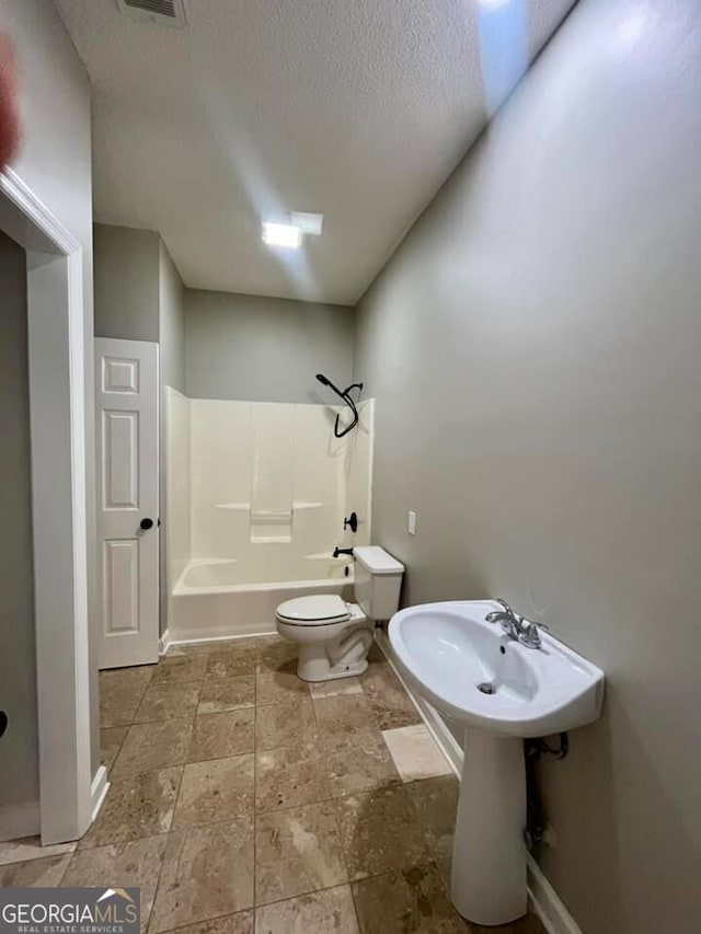 bathroom featuring toilet, shower / tub combination, a textured ceiling, stone finish floor, and baseboards