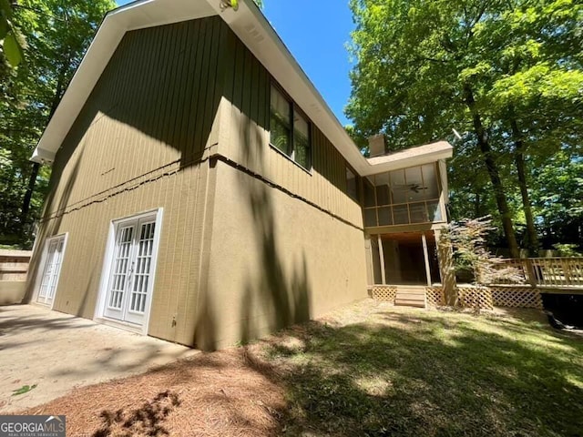 back of property with french doors, a ceiling fan, a wooden deck, a sunroom, and a lawn