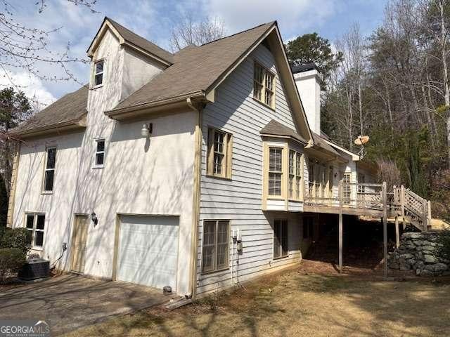 view of property exterior featuring driveway, a wooden deck, stucco siding, a chimney, and a garage