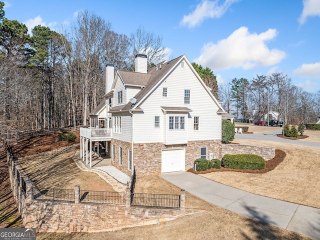 view of side of property with stone siding, concrete driveway, an attached garage, fence private yard, and a chimney