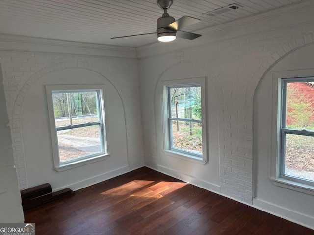 spare room with a healthy amount of sunlight, brick wall, dark wood-style flooring, and ornamental molding