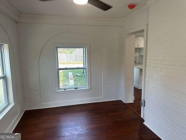 empty room with baseboards, a ceiling fan, brick wall, and dark wood-style flooring