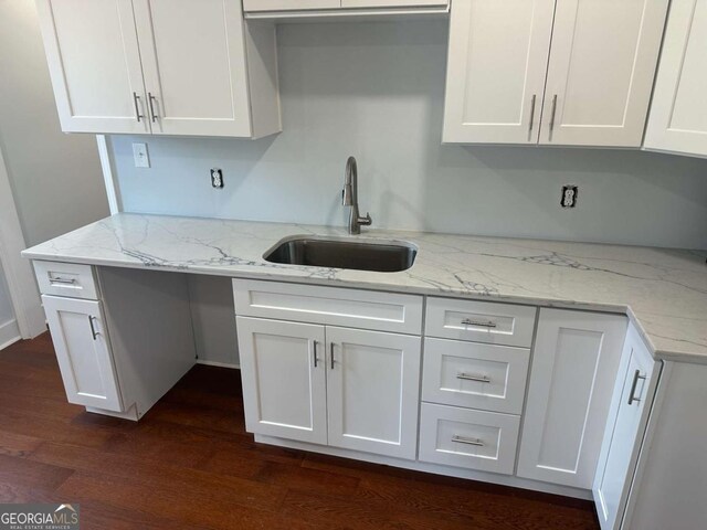 kitchen with a sink, light stone counters, dark wood finished floors, and white cabinetry