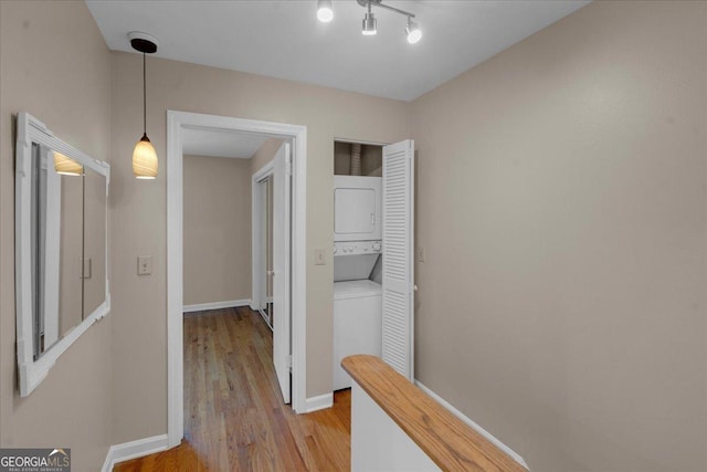 hallway featuring baseboards, stacked washer and clothes dryer, and light wood-type flooring