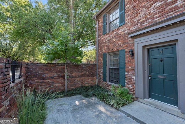 view of exterior entry featuring brick siding and fence