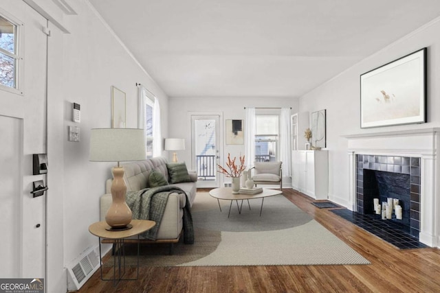 living area with visible vents, a tile fireplace, baseboards, and wood finished floors