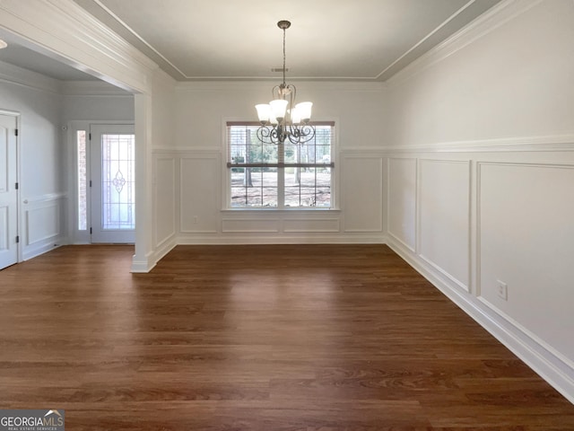 unfurnished dining area featuring a notable chandelier, a decorative wall, crown molding, and dark wood-style flooring