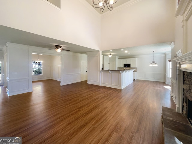 unfurnished living room featuring dark wood-style floors, a fireplace, ornamental molding, a decorative wall, and ceiling fan with notable chandelier