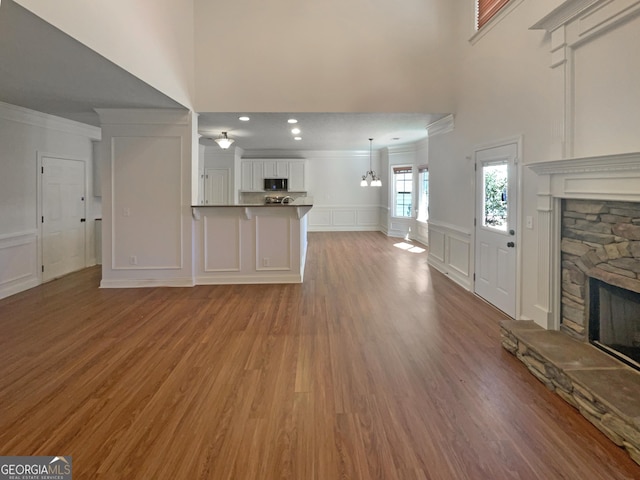 unfurnished living room with wood finished floors, a wainscoted wall, a fireplace, crown molding, and a decorative wall