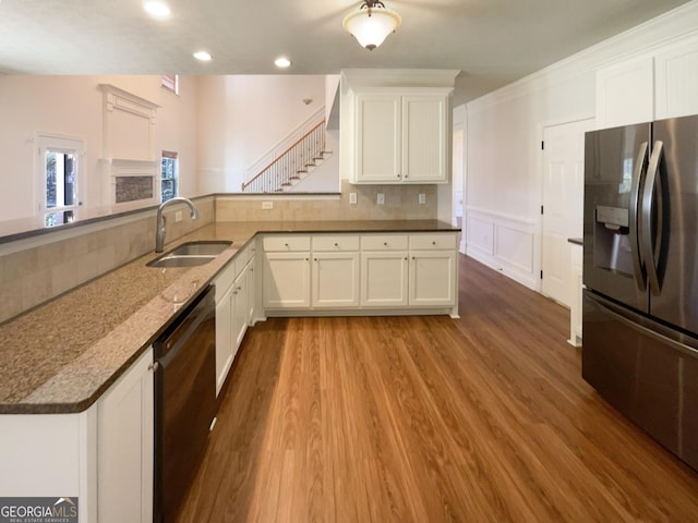 kitchen with dark stone counters, a sink, black dishwasher, light wood-style floors, and stainless steel refrigerator with ice dispenser