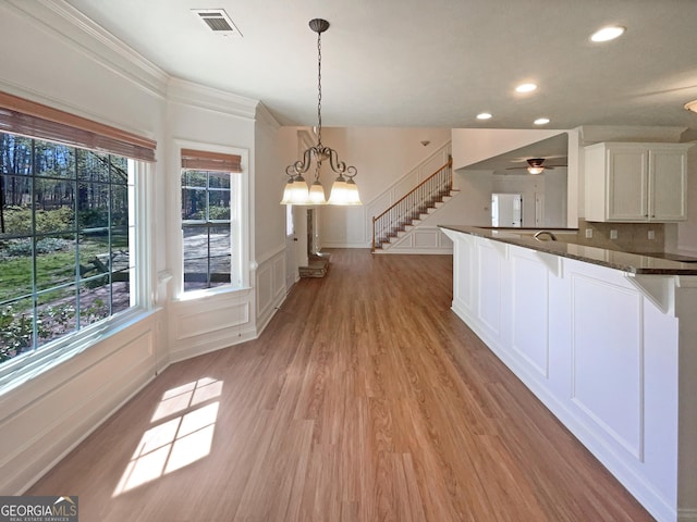 kitchen with visible vents, light wood-style flooring, dark countertops, white cabinetry, and a decorative wall