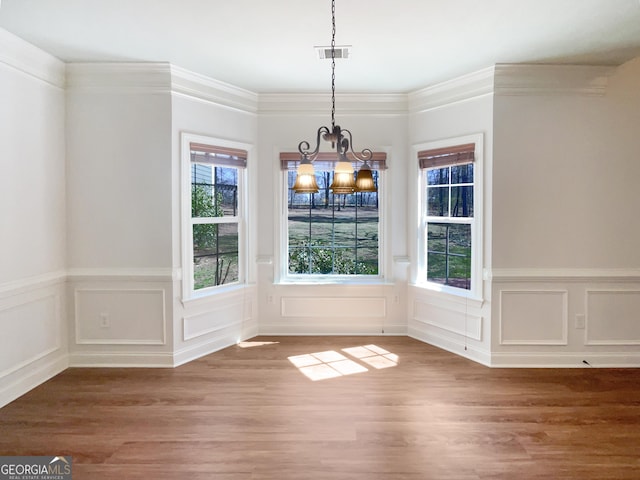 unfurnished dining area with visible vents, a notable chandelier, wood finished floors, and crown molding