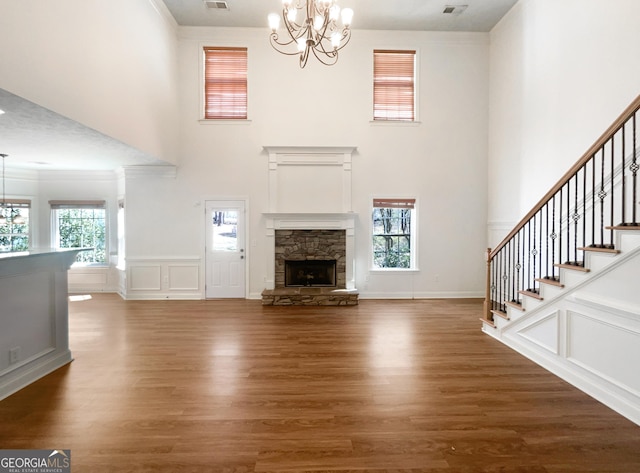 unfurnished living room with visible vents, a stone fireplace, an inviting chandelier, wood finished floors, and a decorative wall