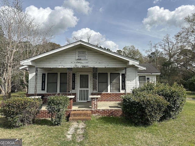 bungalow-style home with a front lawn, brick siding, and covered porch