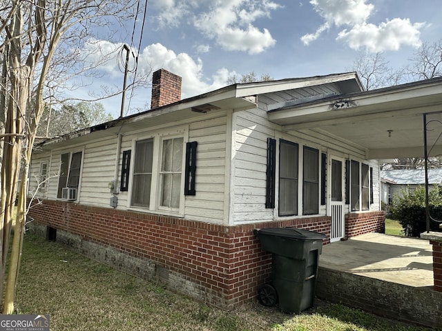 view of home's exterior with brick siding, crawl space, an attached carport, and a chimney