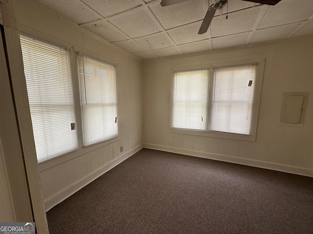 unfurnished room with a drop ceiling, baseboards, dark carpet, and ceiling fan