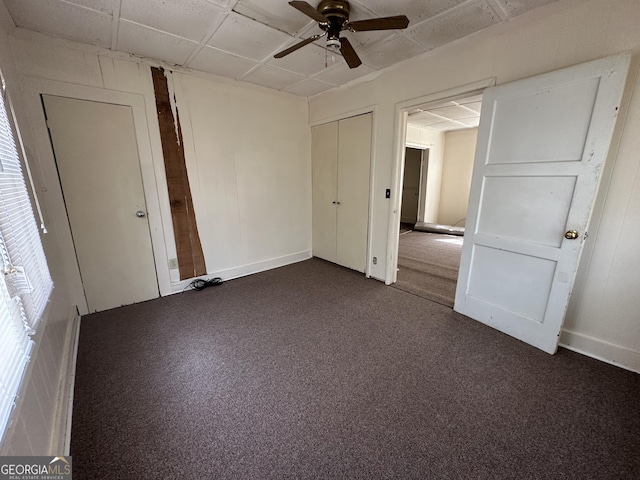 unfurnished bedroom with baseboards, ceiling fan, dark carpet, a closet, and a paneled ceiling