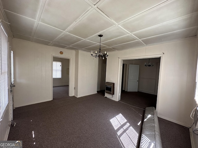 unfurnished living room with a chandelier, heating unit, and dark colored carpet