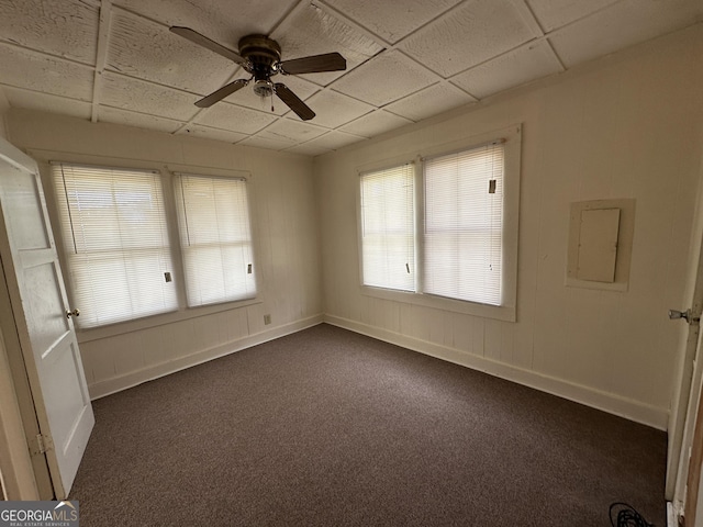 empty room featuring baseboards, ceiling fan, electric panel, a paneled ceiling, and dark colored carpet