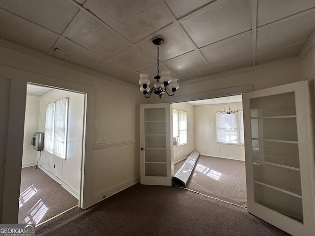 unfurnished dining area with a notable chandelier, baseboards, carpet floors, and ornamental molding